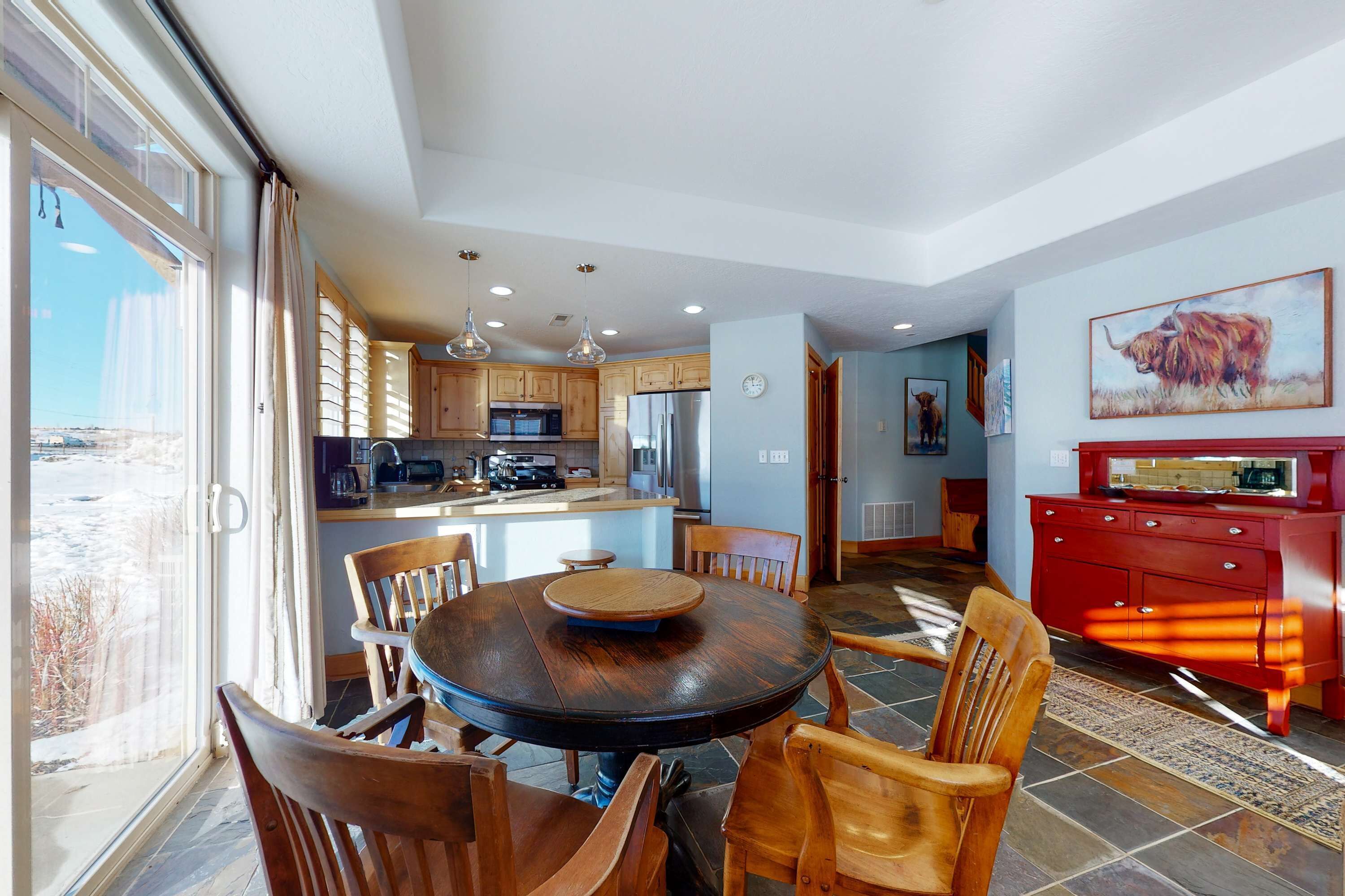 A spacious kitchen with wooden cabinets, a dining area with a round table and chairs, and a red dresser.
