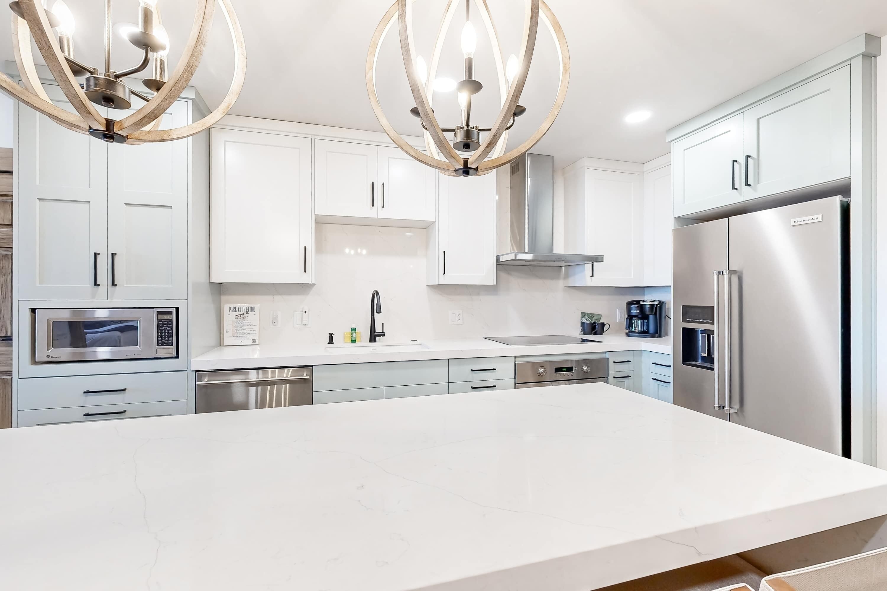 A modern kitchen with white cabinetry, stainless steel appliances, and a large island.