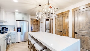 A modern kitchen with a central island, stainless steel appliances, wooden cabinets, and a chandelier. - Ski-in-ski-out condo - indoor & outdoor pools, sauna, hot tubs, game room, gym, W&D, AC (Park City)