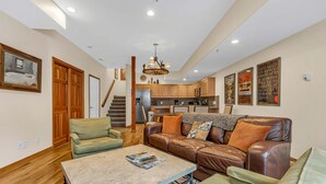 A spacious living area with a sofa, a coffee table, and a kitchen in the background. - Lovely home with gas fireplaces, patio, hot tub, & WiFi - great location (Park City)