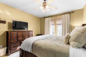 A bedroom with a bed, a television on a wooden dresser, a ceiling fan, and a window with curtains. - Spacious Redstone Home with Fireplace, Patio & Walk to Dining (Park City)