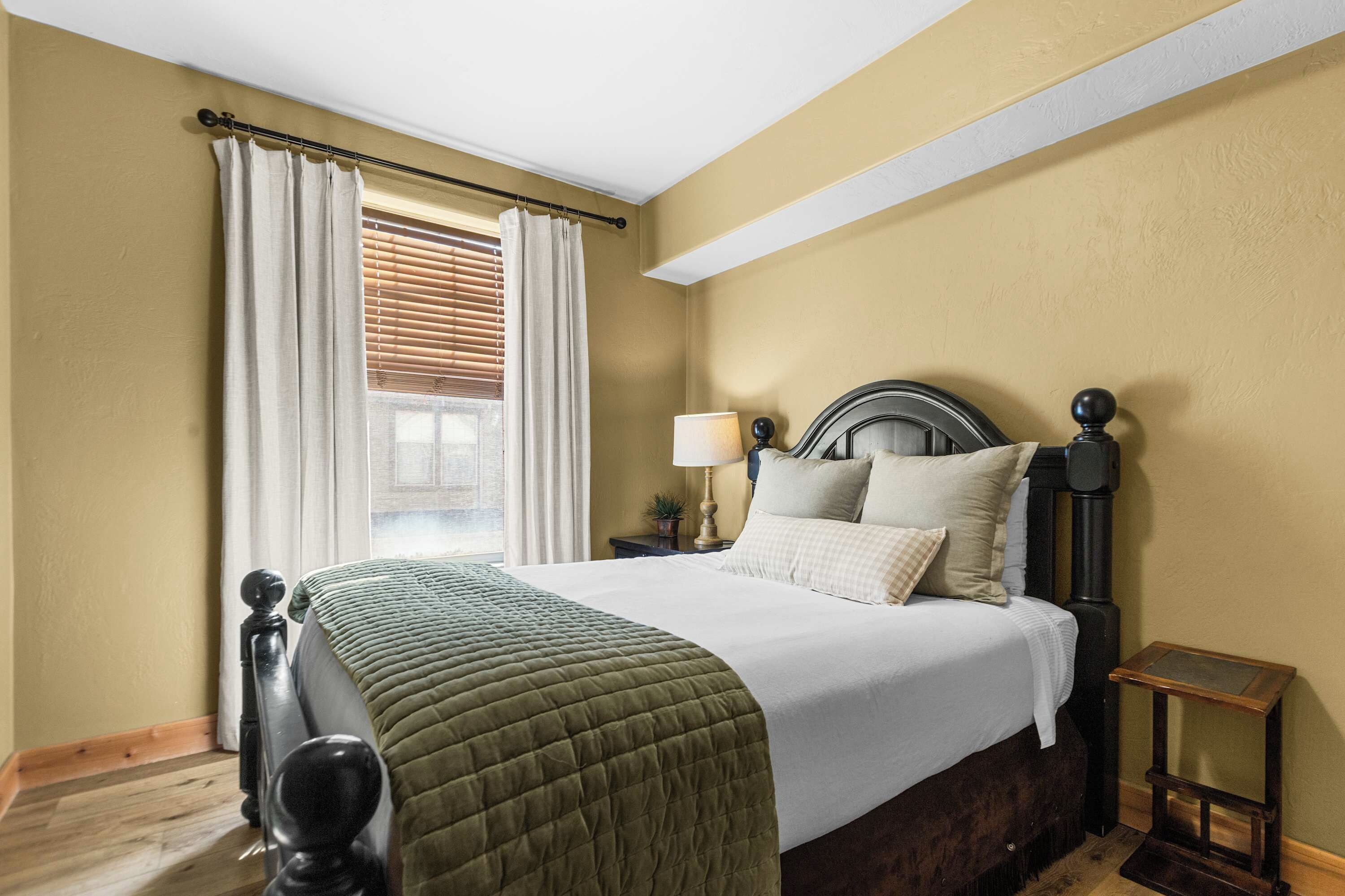 A bedroom with a bed, curtains, a nightstand, a lamp, and a small table.