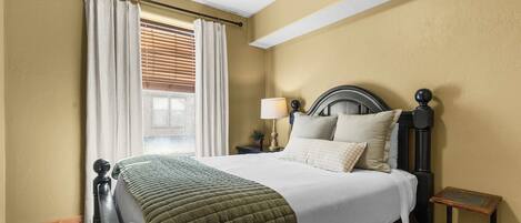 A bedroom with a bed, curtains, a nightstand, a lamp, and a small table.