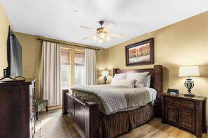 Une chambre à coucher avec un lit, un ventilateur de plafond, une table de chevet avec une lampe, une commode et un tableau au mur.