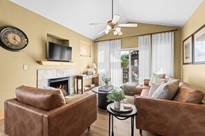 Un salon avec des canapés en cuir, une cheminée, un téléviseur et un ventilateur de plafond.