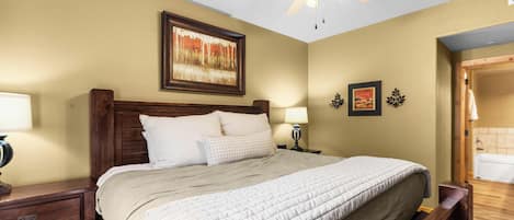 A bedroom with a bed, a nightstand, a lamp, a ceiling fan, and a painting on the wall.
