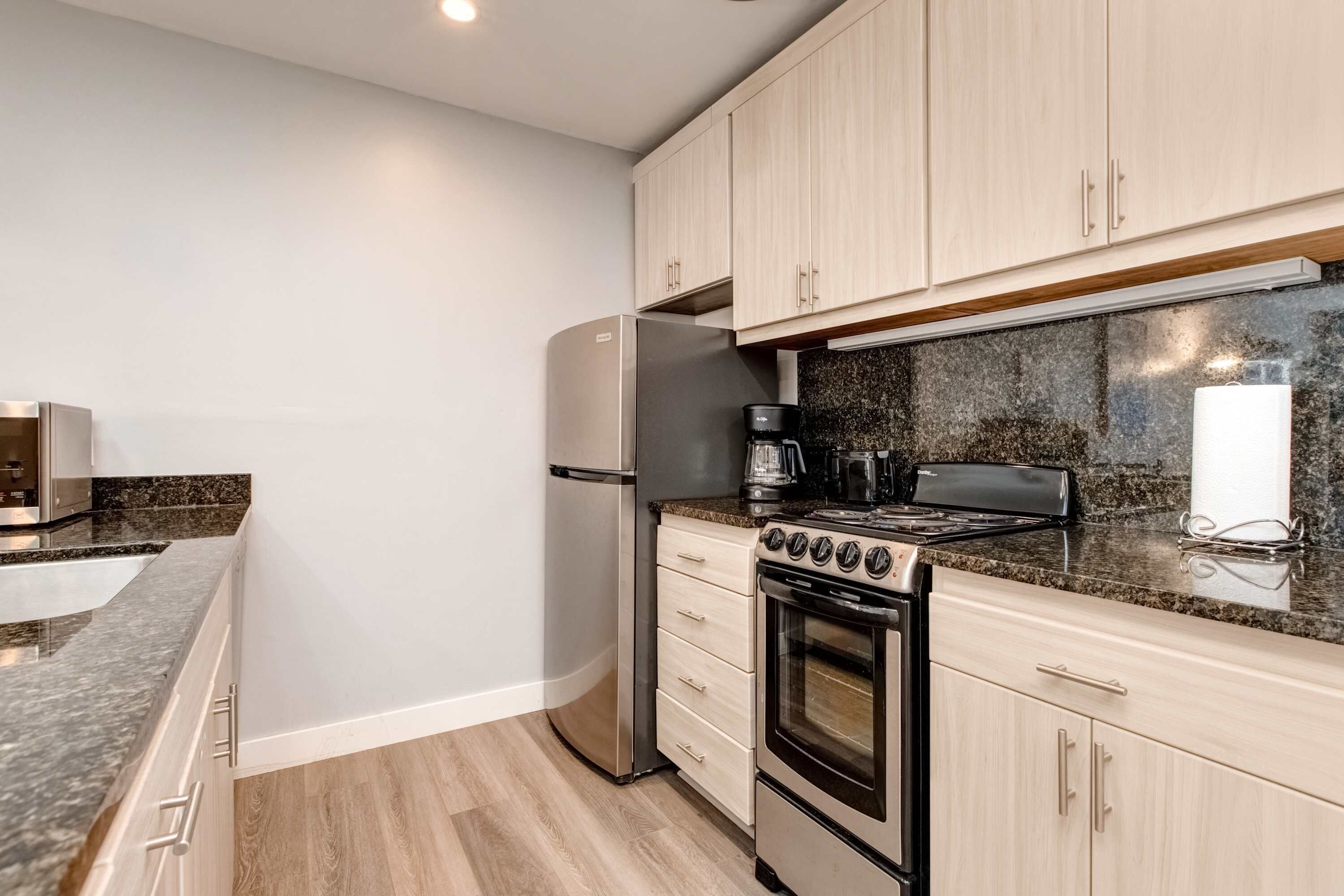 A kitchen with a stainless steel refrigerator, a stove, and a coffee maker.