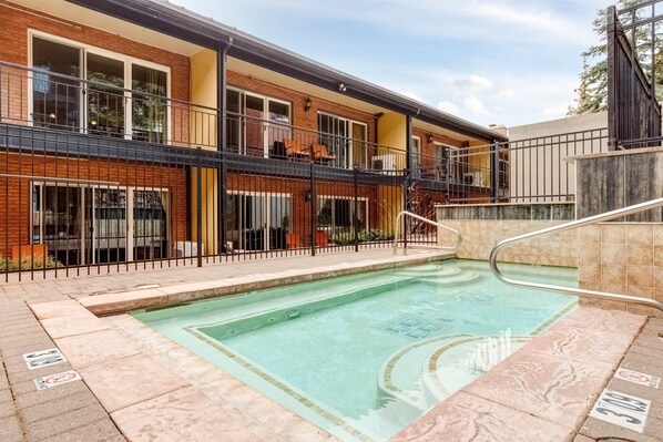 A swimming pool with a tiled deck, a brick building with balconies, and a gated entrance. - Main Street condo with AC, balcony, on-site dining, hot tub, & firepit (Park City)