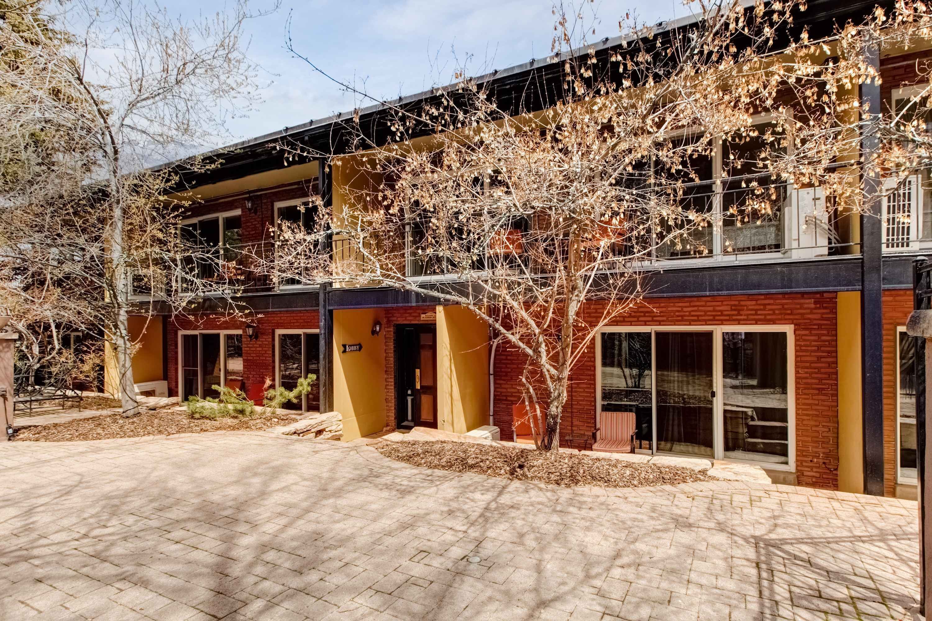 A building with a brick facade, large windows, and a covered outdoor area with a tree.