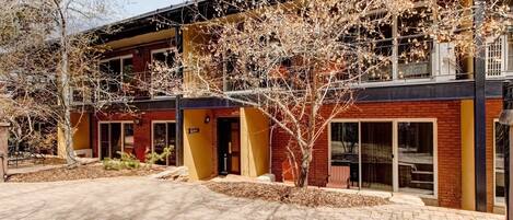 A building with a brick facade, large windows, and a covered outdoor area with a tree.