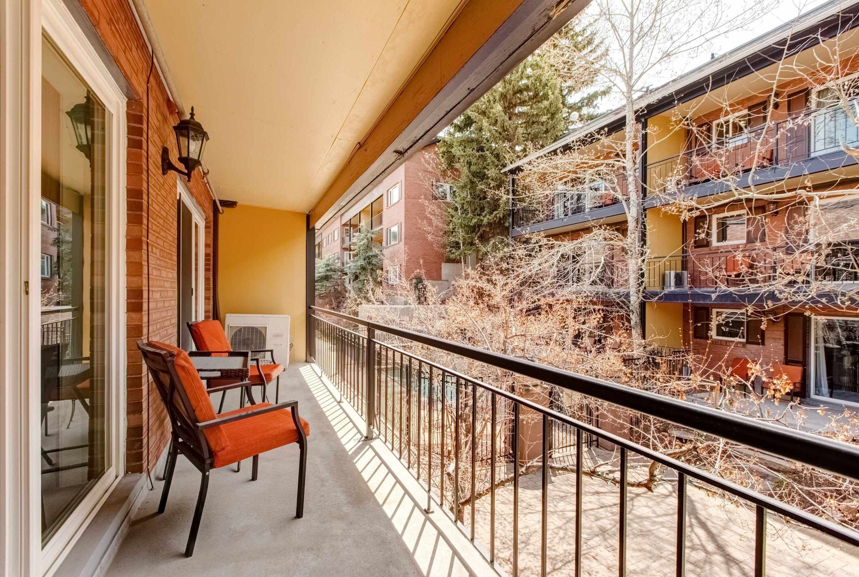 Un balcon avec des chaises, une table et une vue sur un immeuble à plusieurs étages, entouré d’arbres.