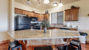 Una cocina con encimeras de granito, armarios de madera, un refrigerador negro, un microondas y una isla grande con taburetes de bar.