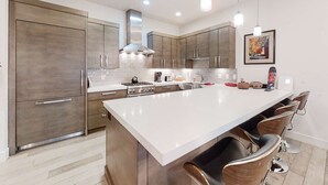 A modern kitchen with a large island, stainless steel appliances, and bar stools. - Posh Condo - Private Hot Tub, Saltwater Pool & Mountain Views (Park City)