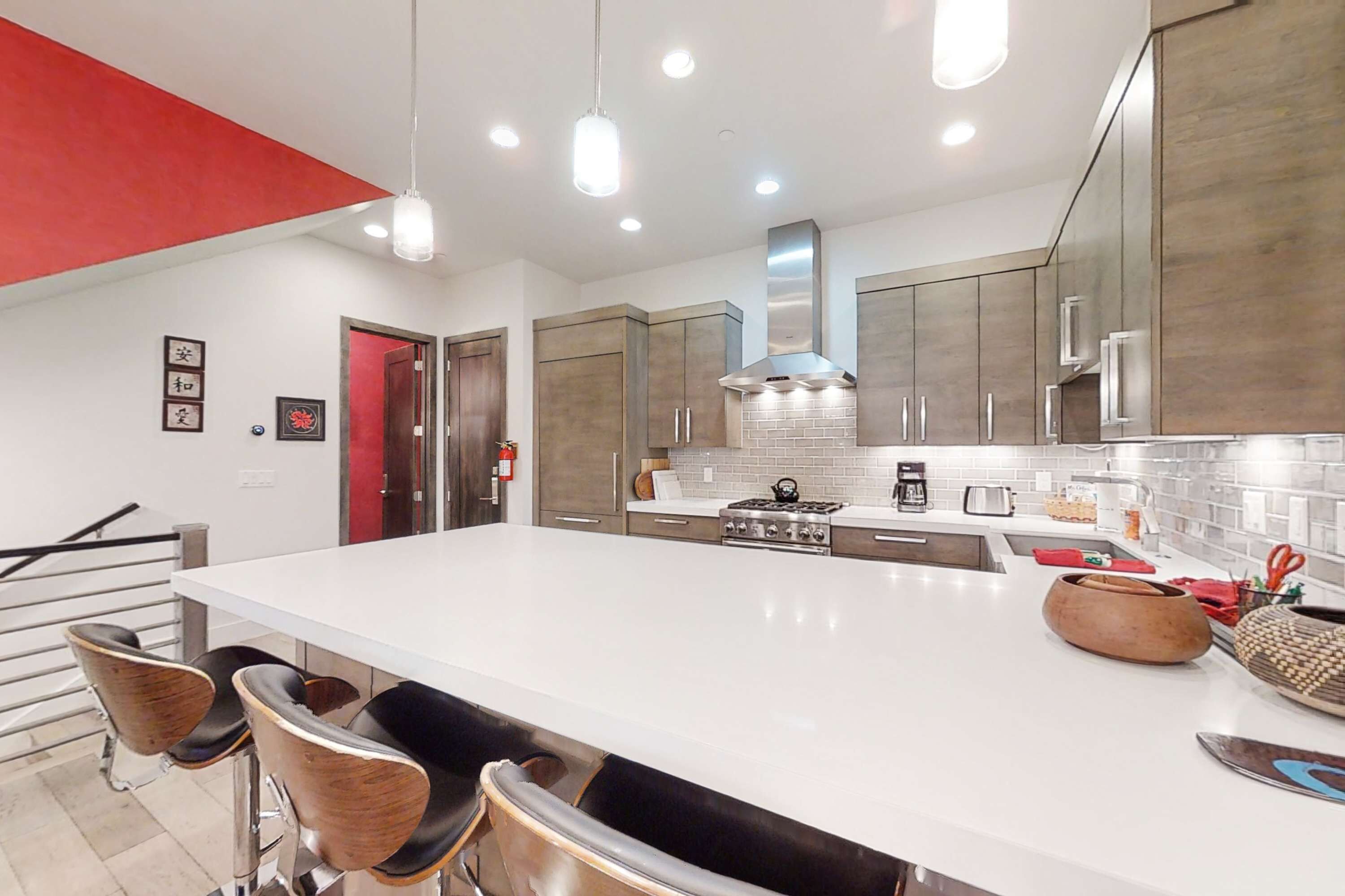 A modern kitchen with a large island, stainless steel appliances, and a red accent wall.