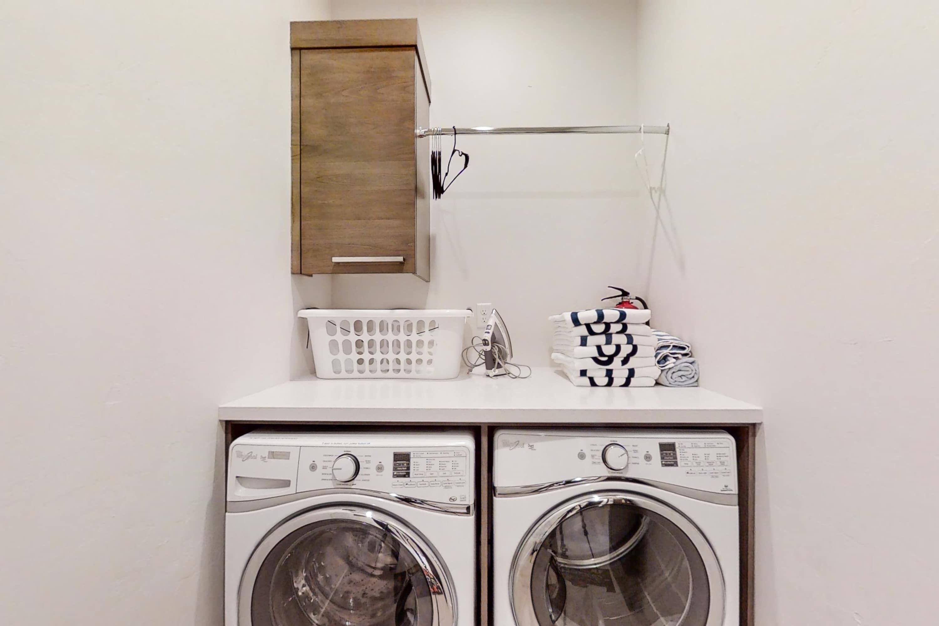 A laundry area with two front-loading washing machines, a wooden cabinet, a drying rack, and a white laundry basket.