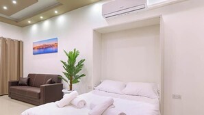A hotel room with a bed, a sofa, a potted plant, and an air conditioning unit. - Elegant Seafront Duplex with Stunning Panoramic Views (Birżebbuġa)