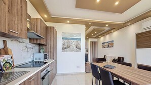 A modern kitchen with wooden cabinets, a microwave, and a dining area with a table and chairs. - Elegant Seafront Duplex with Stunning Panoramic Views (Birżebbuġa)