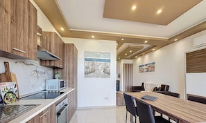 A modern kitchen with wooden cabinets, a microwave, and a dining area with a table and chairs. - Elegant Seafront Duplex with Stunning Panoramic Views (Birżebbuġa)