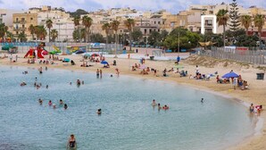 A beach with people swimming and sunbathing, a lifeguard tower, and buildings in the background. - Elegant Seafront Duplex with Stunning Panoramic Views (Birżebbuġa)