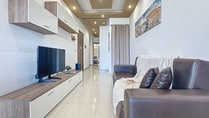 A modern living room with a flat-screen TV, a sofa, a coffee table, and a painting on the wall. - Elegant Seafront Duplex with Stunning Panoramic Views (Birżebbuġa)