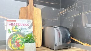 Un piano di lavoro in cucina con un libro di ricette, un tagliere di legno, un tostapane e una pianta in vaso.