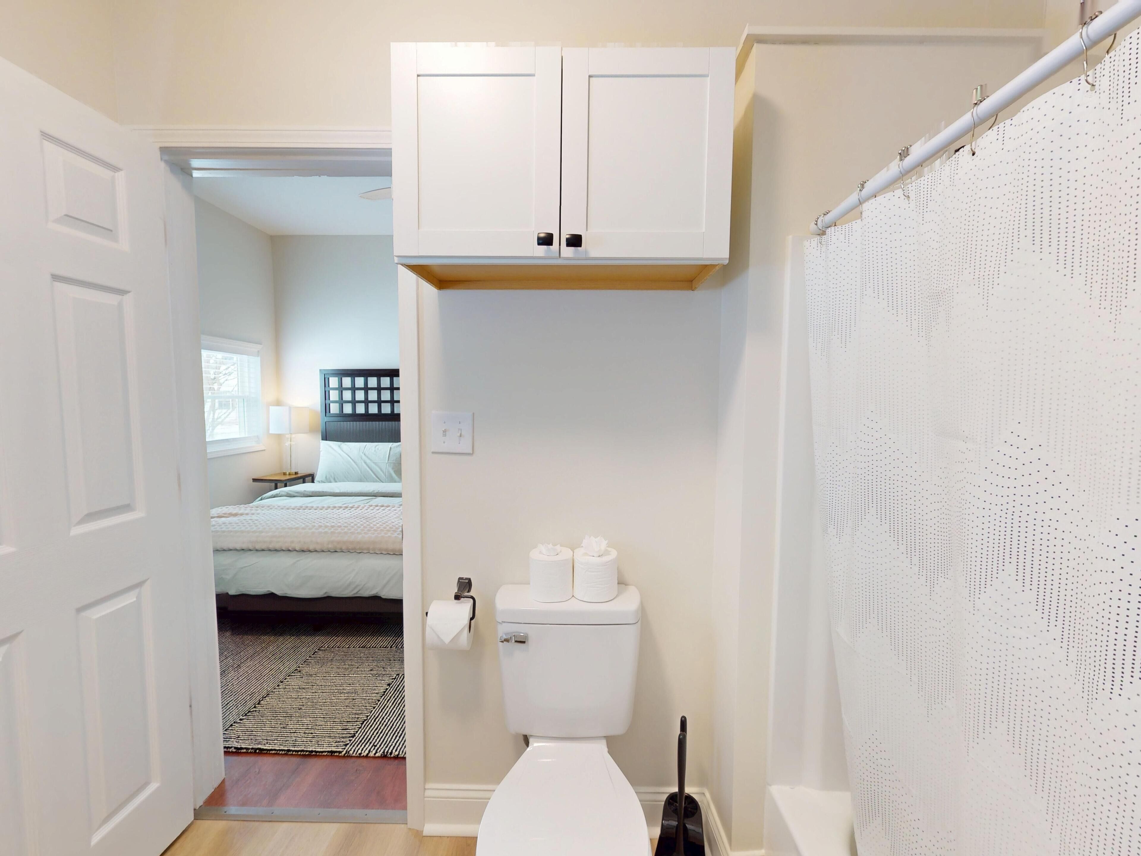 Een badkamer met toilet, douchegordijn en raam.