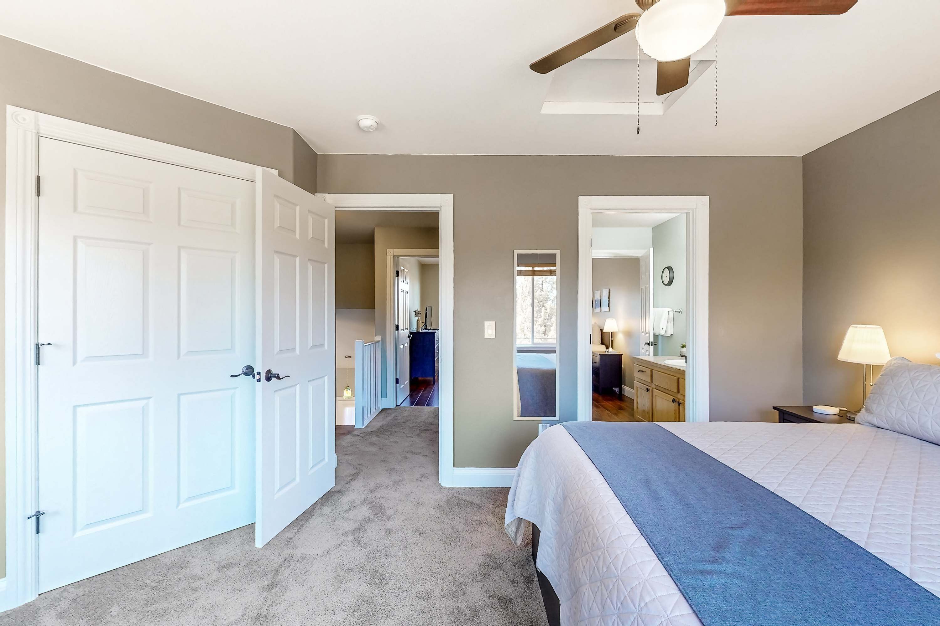A bedroom with a bed, a nightstand, a lamp, a mirror, and a door leading to another room.