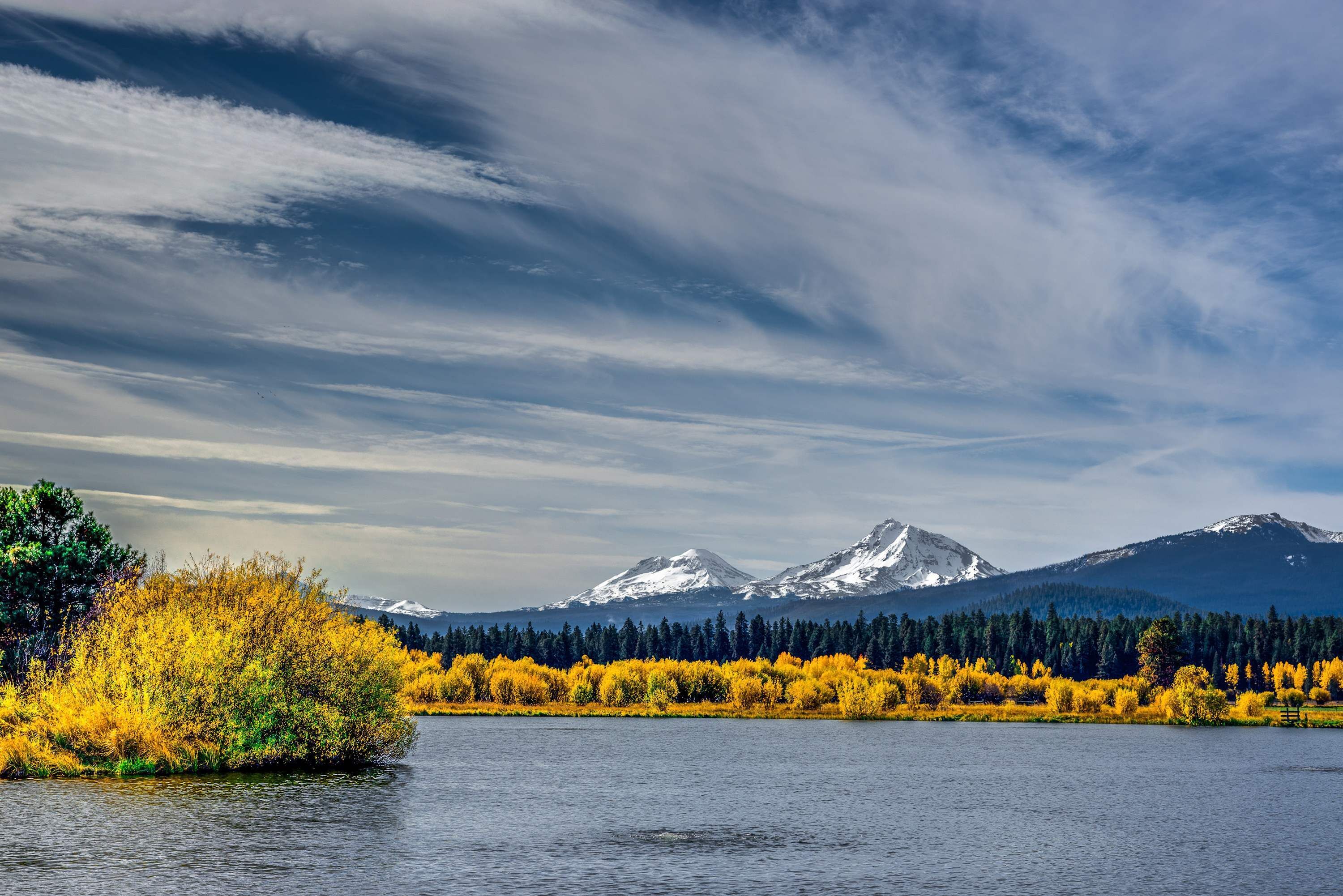 Un lago con montañas al fondo y árboles de hojas amarillas.