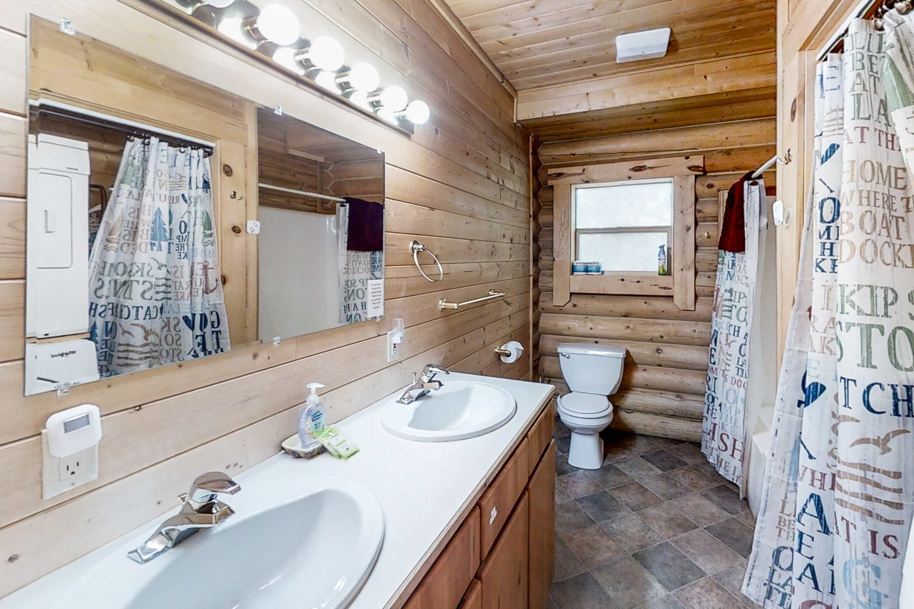 A wooden cabin bathroom with two sinks, a toilet, and a shower curtain with text.