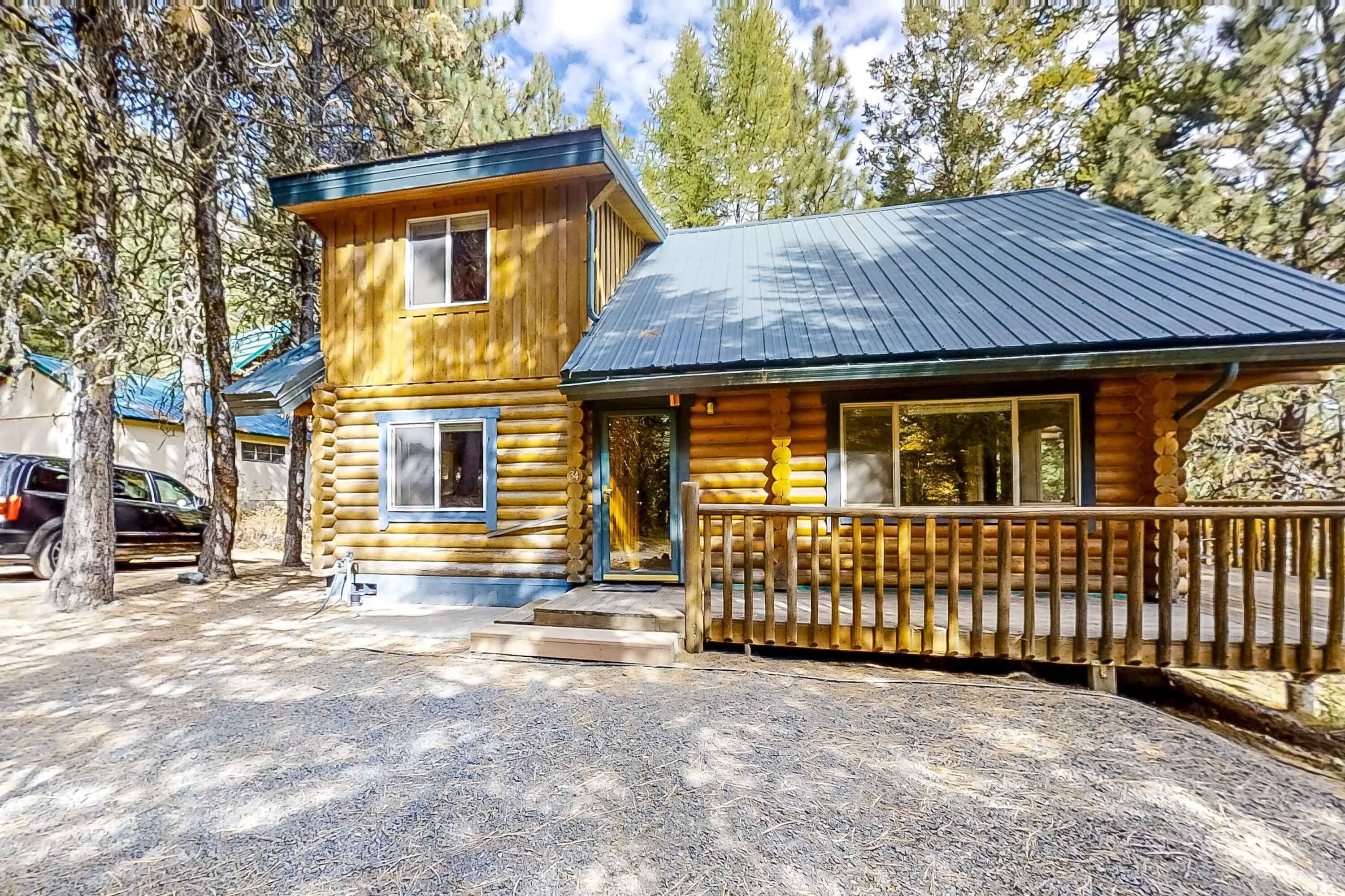 Eine Blockhütte mit Veranda und Metalldach, umgeben von Bäumen.