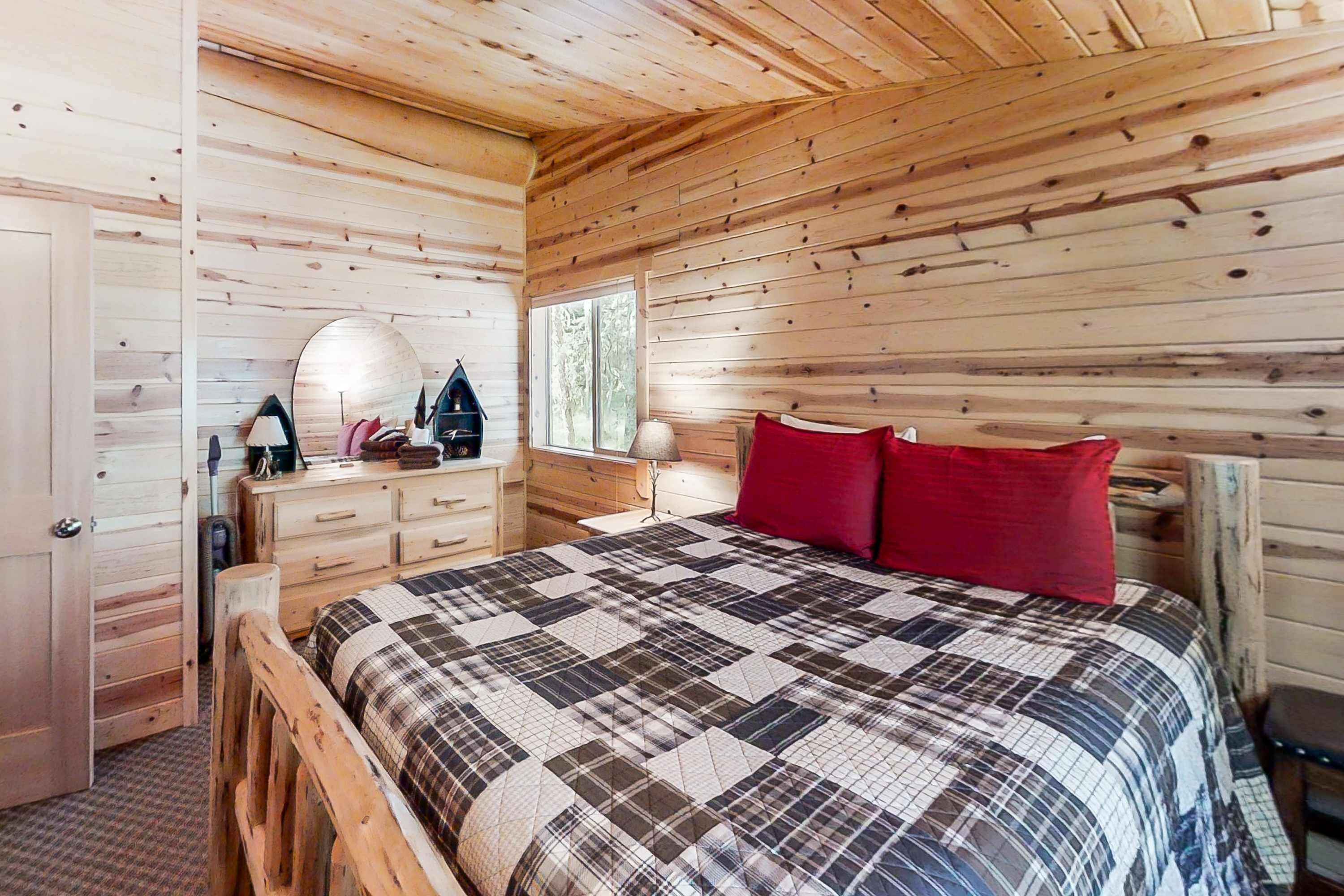 A wooden-paneled room with a bed, dresser, and a mirror.