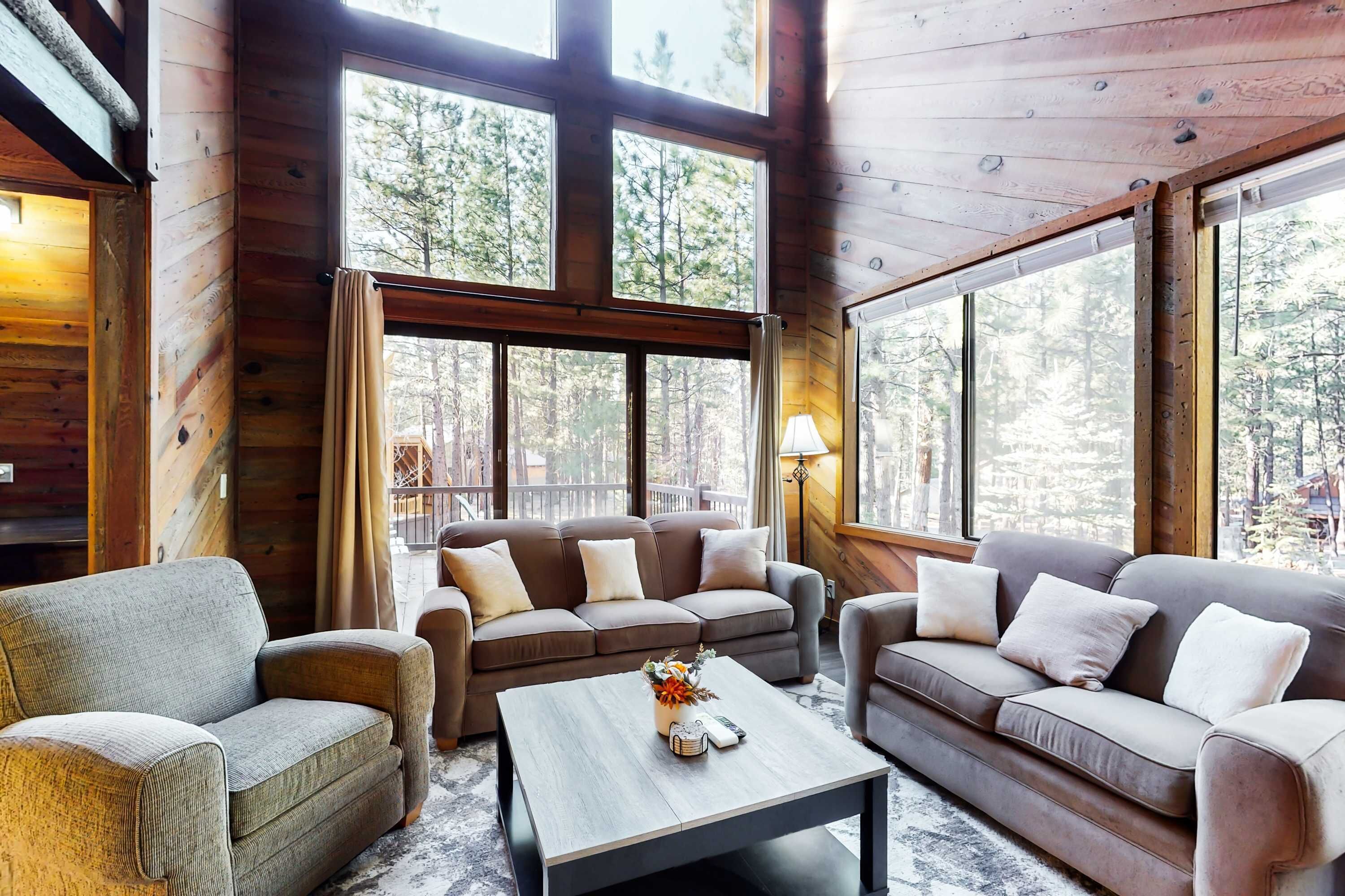 A cozy cabin interior with large windows, a sofa set, and a coffee table.