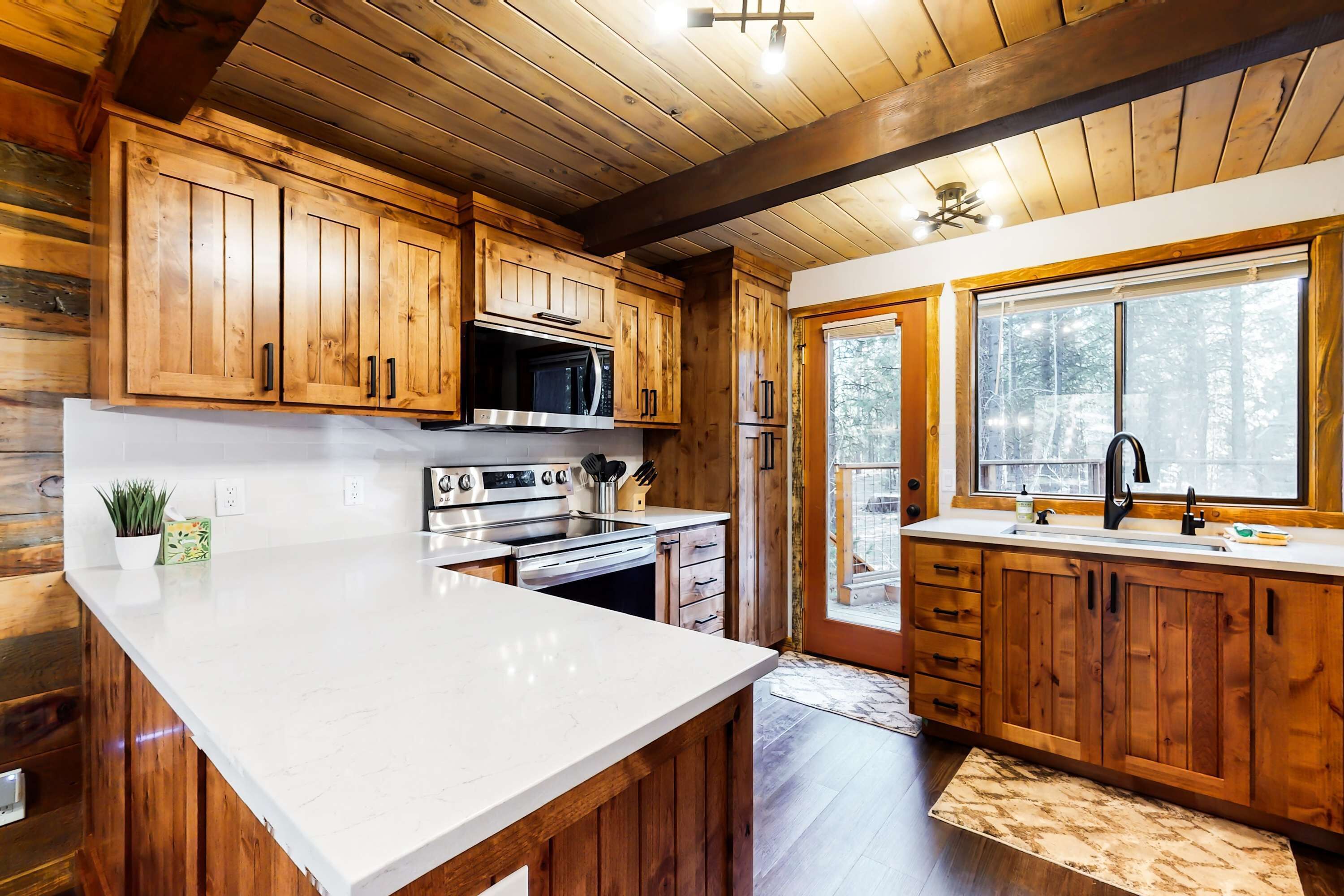 A kitchen with wooden cabinets, a white countertop, a microwave, a stove, and a sink.