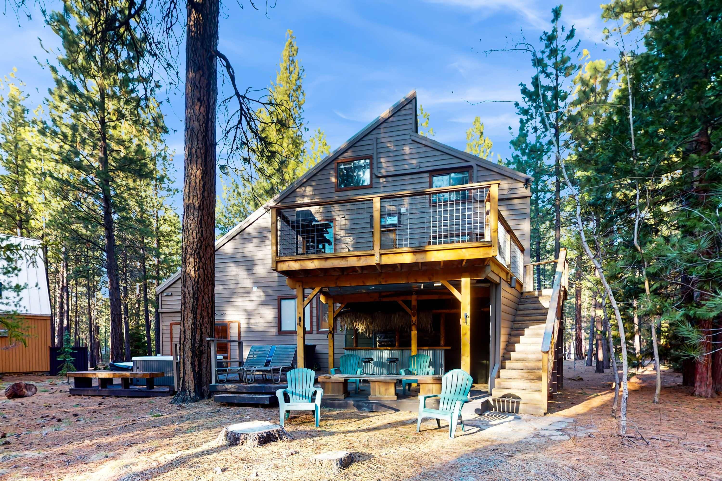 A two-story log cabin with a balcony, outdoor seating, and a forested backdrop.