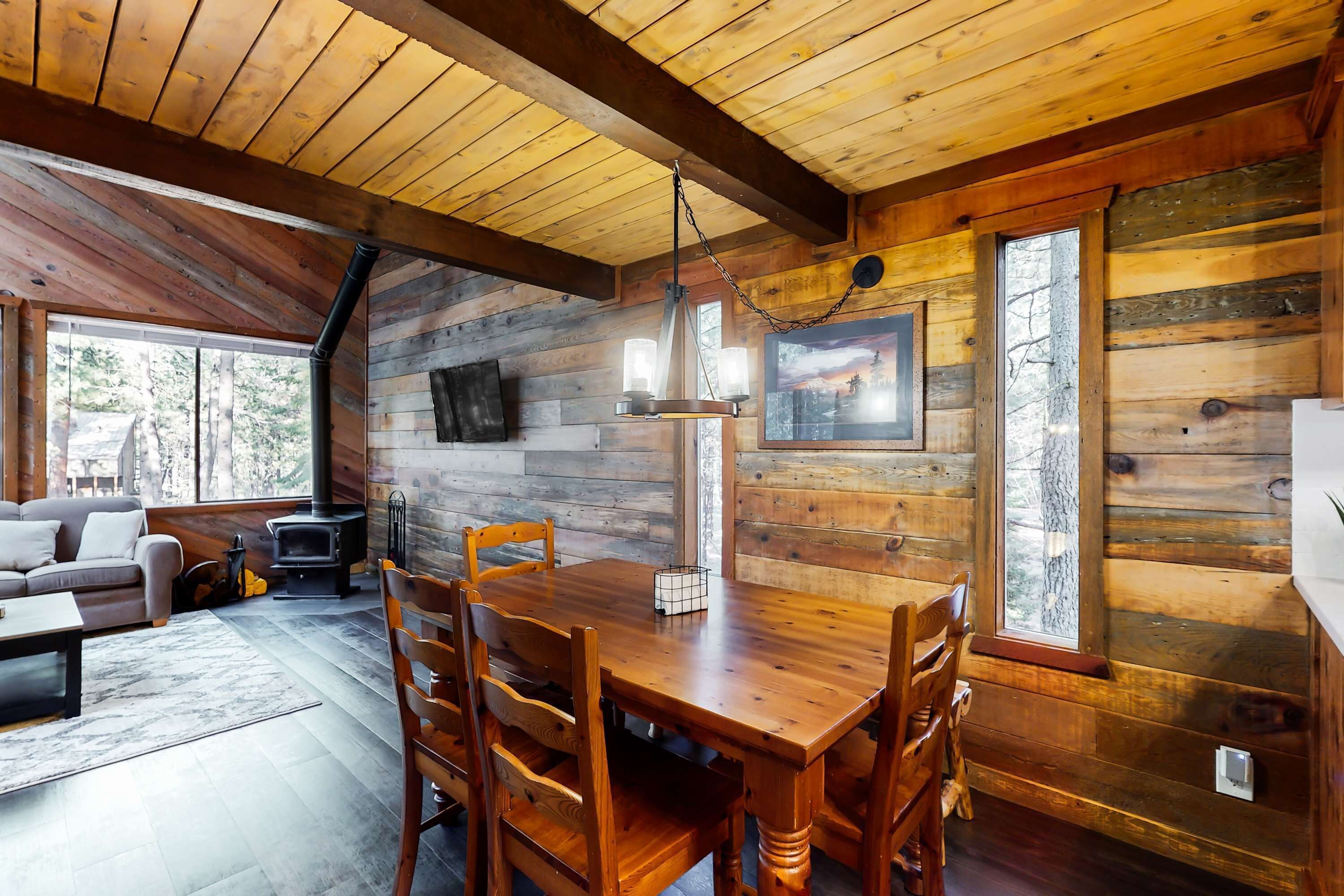 A wooden cabin interior with a dining table, chairs, a sofa, a fireplace, and a television.