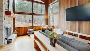A spacious living room with a large window, a fireplace, a sofa, and a flat-screen TV. - Spacious family friendly home with fireplace, full kitchen, deck, grill & WIFI (Black Butte Ranch)