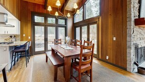 A wooden dining area with a large table and chairs, a kitchen with a stove, and a stone fireplace. - Spacious family friendly home with fireplace, full kitchen, deck, grill & WIFI (Black Butte Ranch)
