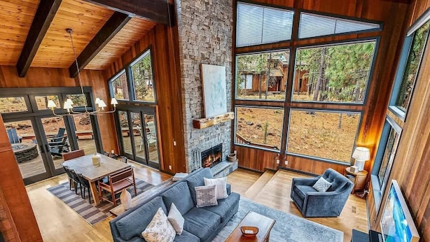 A spacious living area with a fireplace, large windows, and a stone wall. - Spacious family friendly home with fireplace, full kitchen, deck, grill & WIFI (Black Butte Ranch)
