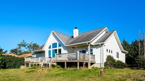 A two-story house with a balcony, a chimney, and a grassy yard. - Ocean view home withhuge deck & yard, hot tub, firepit & game room - dogs OK (Newport)