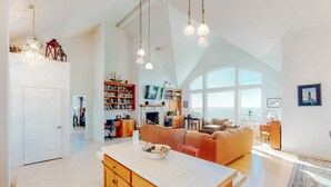 A spacious living area with a large window, a kitchen island, and a cozy seating area. - Ocean view home withhuge deck & yard, hot tub, firepit & game room - dogs OK (Newport)