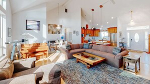 A spacious living room with a sectional sofa, a wooden coffee table, and a large window providing natural light. - Ocean view home withhuge deck & yard, hot tub, firepit & game room - dogs OK (Newport)