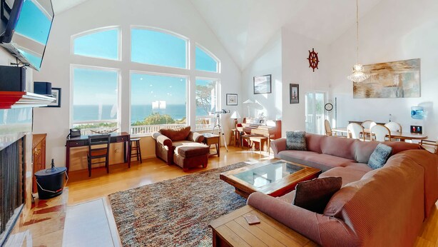 A spacious living area with a large window, a cozy seating area, and a dining setup. - Ocean view home withhuge deck & yard, hot tub, firepit & game room - dogs OK (Newport)