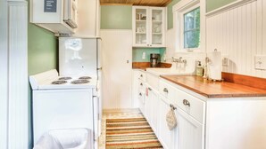 Una cucina compatta con mobili bianchi, un fornello e un piano di lavoro in legno.