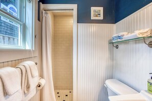 Un baño con inodoro, estante de vidrio con toallas, cortina de ducha y ventana.