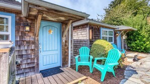 Una casa di legno con una porta blu, due poltrone Adirondack color turchese e un vialetto in pietra.