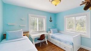 Habitación con dos camas, un escritorio y una silla. Cuenta con ventanas con persianas, una lámpara de techo y un adorno fijado a la pared.