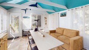 Una habitación con techo blanco, sofá color beige, una mesa blanca y una puerta con vistas.