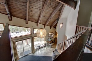 A wooden ceiling, a dining area with chairs, a hanging light fixture, and a staircase.