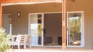 A covered outdoor area with a sliding glass door leading to a room, a small table with chairs, and a potted plant. - Rissie's 3 Bedroom Apartment (Cape Town)