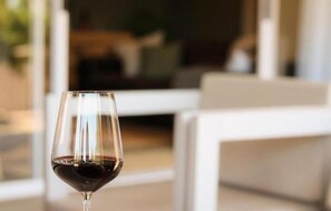 A wine glass with a dark liquid, likely wine, in a modern interior setting with white furniture. - Rissie's 3 Bedroom Apartment (Cape Town)